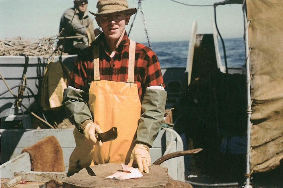 man on boat in red plaid shirt and tan apron prepares a halibut stomach as bait on a wooden surface