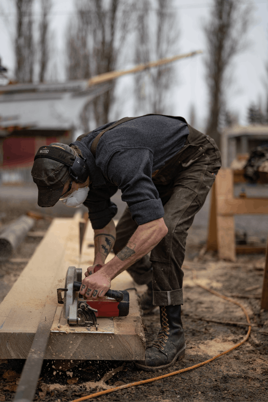 man with hearing protection on cutting a board with a hand saw outside