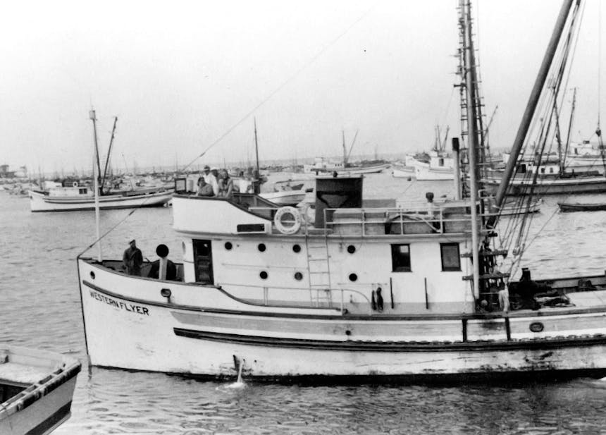 black and white image of boats anchored in a harbor. Small double deck fishing vessel named 