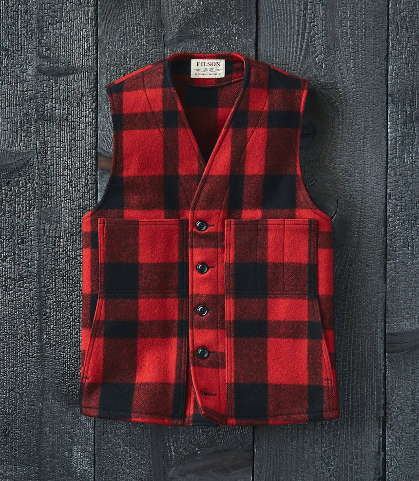 a top down view of a red and black mackinaw wool vest laid on a wood