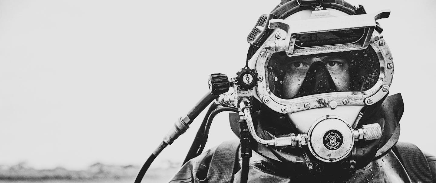 black and white chest-up image of person wearing scuba gear standing above water