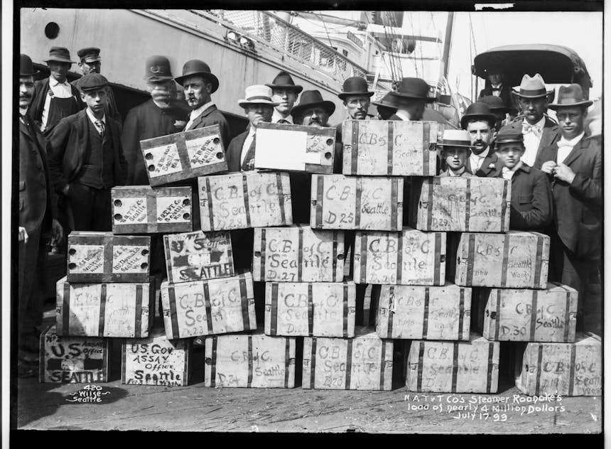 Men in suits and some police officers standing behind a stack of boxes reading CB of C Seattle