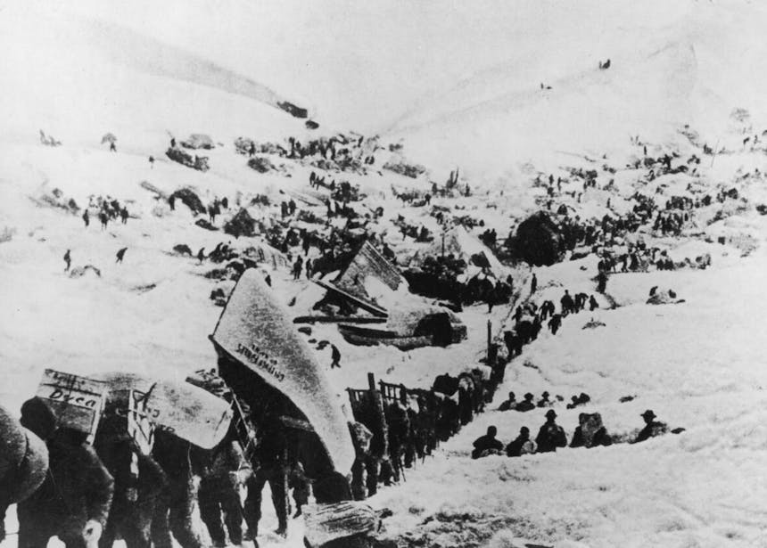long line of people walking through a snowy mountainous area carrying canoes and other supplies on their backs
