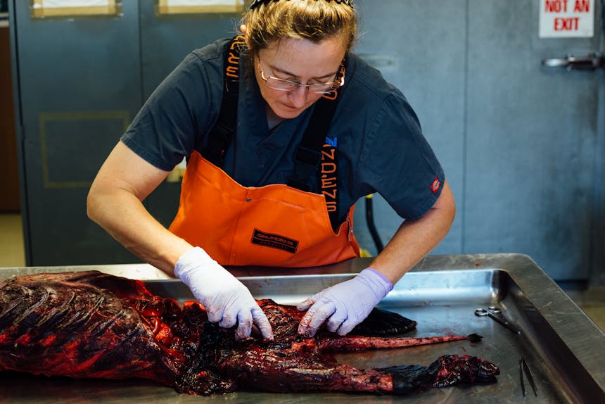 woman working on a carcass of an animal on top of a stainless steel table
