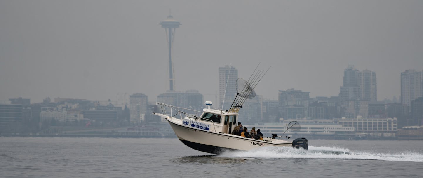 speed boat with many fishing rods and a fishing net speeds across the puget sound with seattle skyline in background