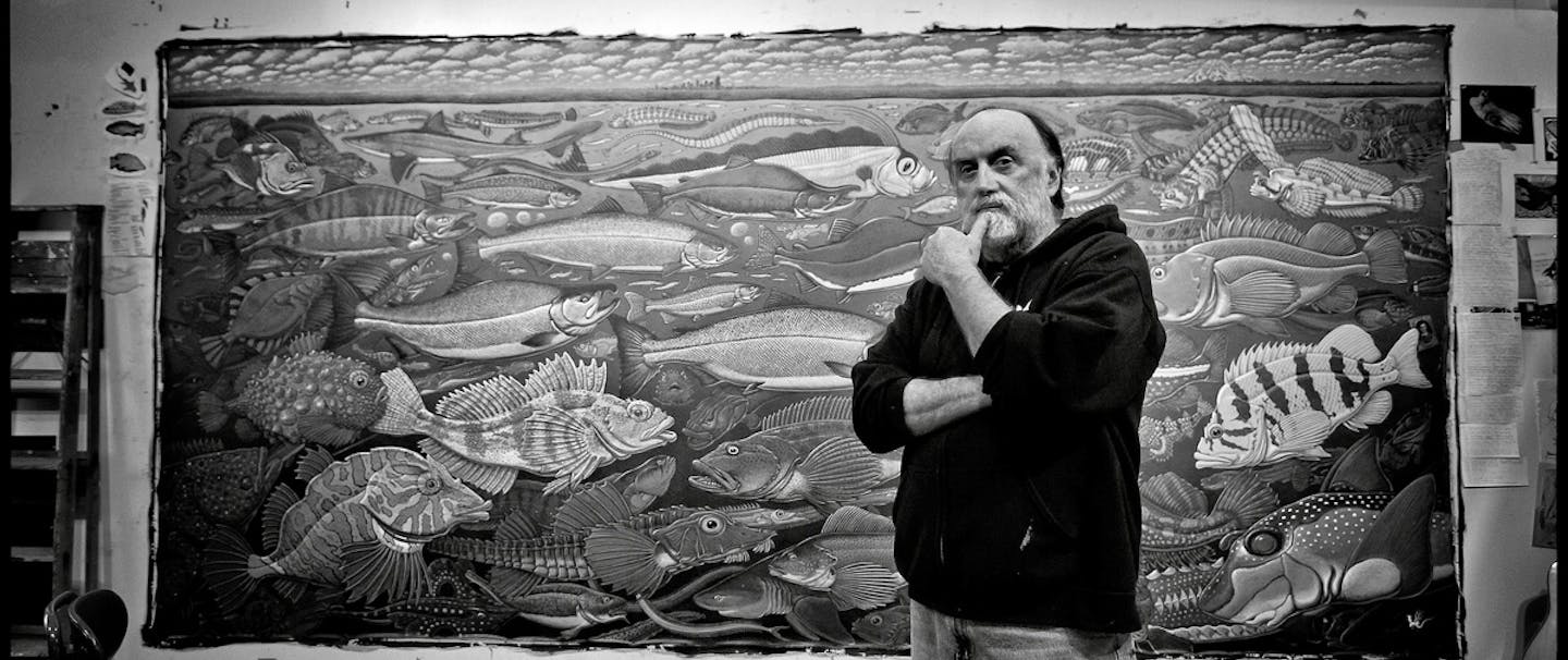 man with white beard standing in front of a large mural detailing many different kinds of exotic fish