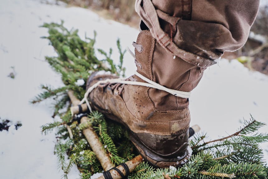 brown boot with hand made snowshoes made out of pine boughs lashed with cord