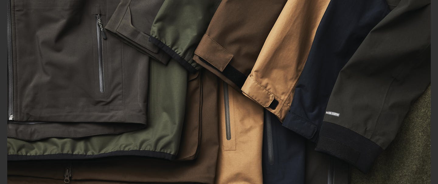filson rain proof jackets laid out on cloth surface various colorways olive green, tan, navy, brown, etc.