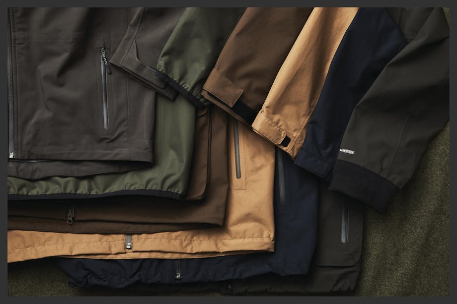 filson rain proof jackets laid out on cloth surface various colorways olive green, tan, navy, brown, etc.