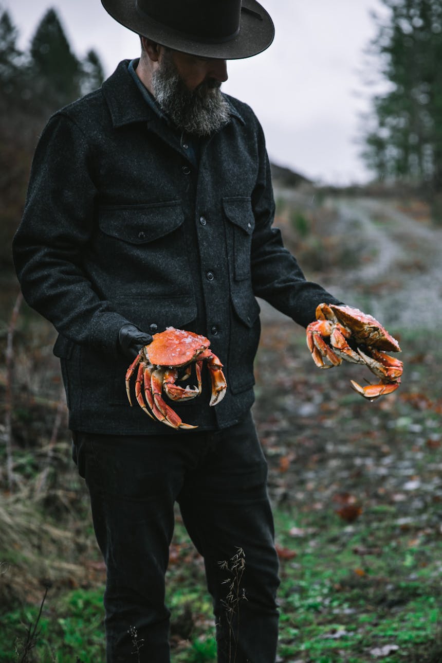 man in flannel shirt and olive wool hat holding two large cooked crabs in both hands
