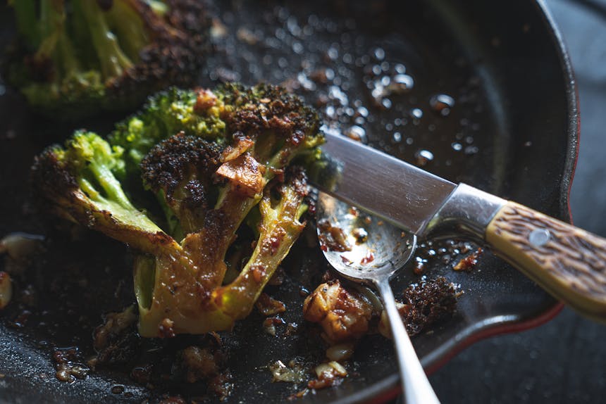 knife and spoon set to the side of a pan containing roasted broccoli