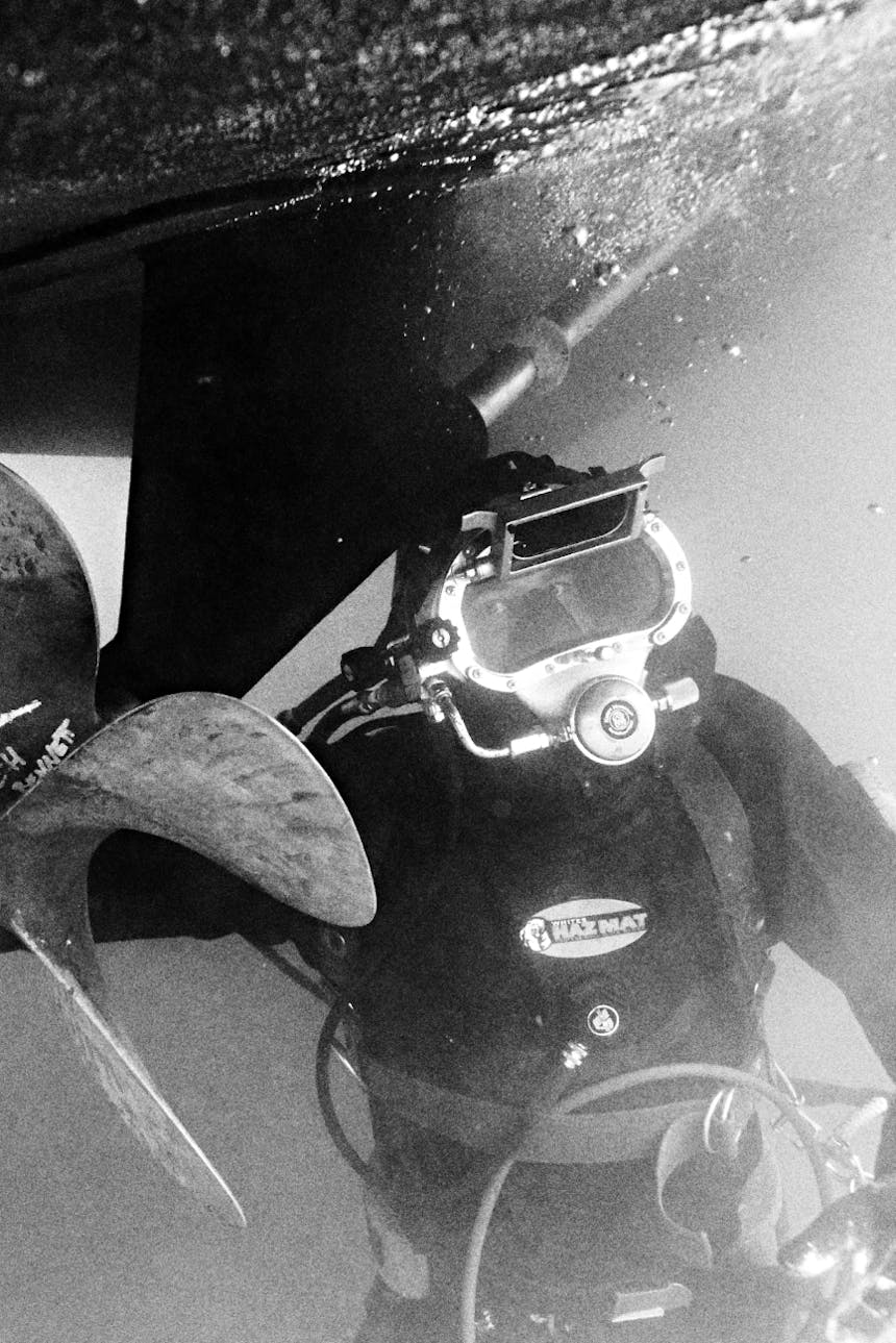 black and white image of person in scuba gear working on propeller of boat underwater