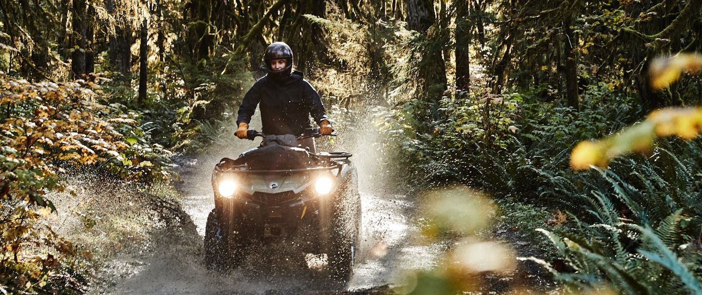 man driving atv splashing through puddle on dirt road in a mossy forest