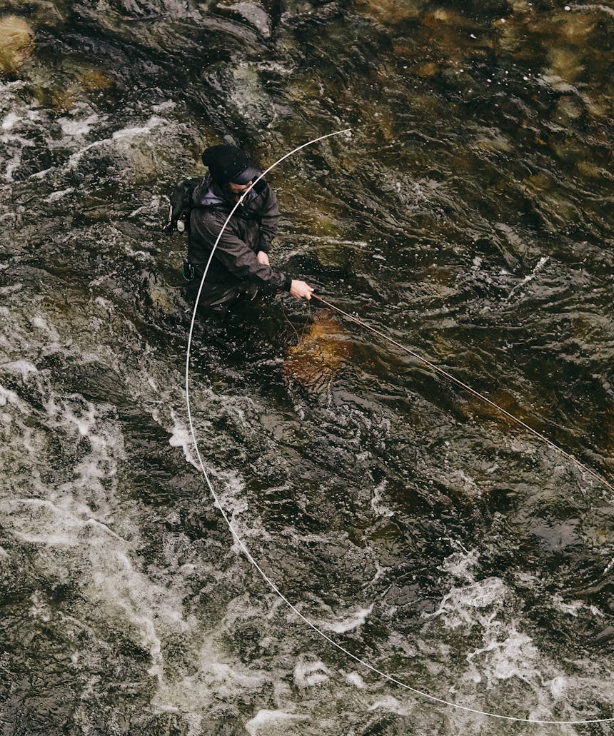 man standing in dark river water casting his fly fishing rod