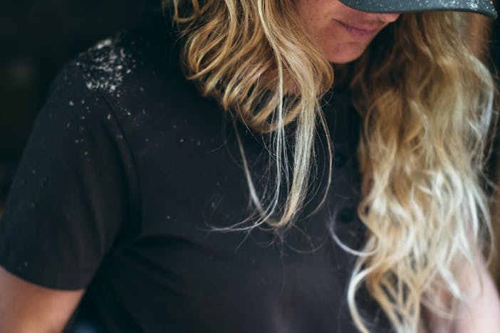 blonde woman in green filson hat and black shirt with some white dust on the shoulder and bill of the cap