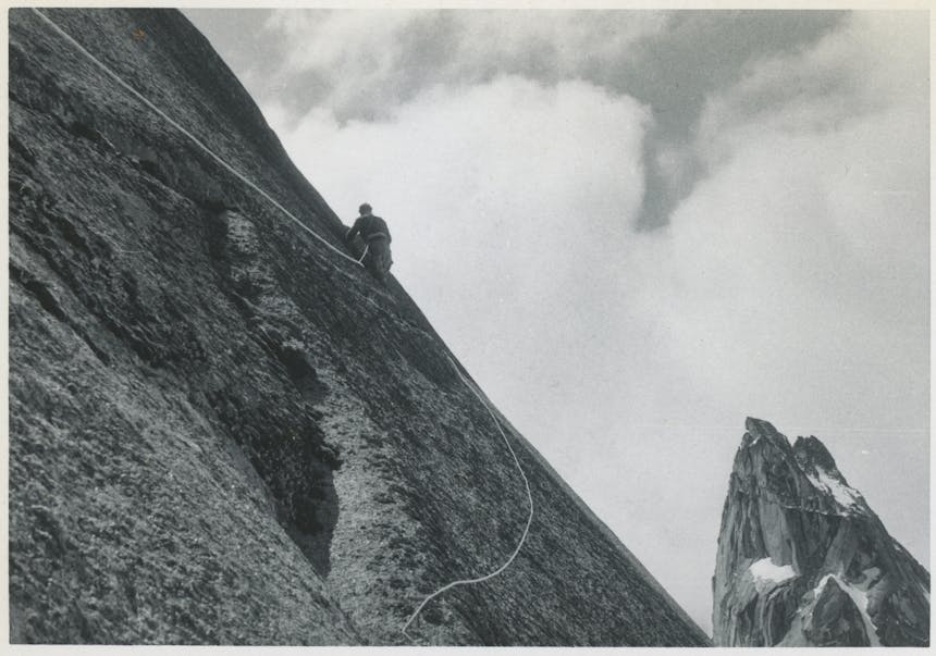 black and white image of an early mountain climber tied to a rope on a sheer granite mountain face