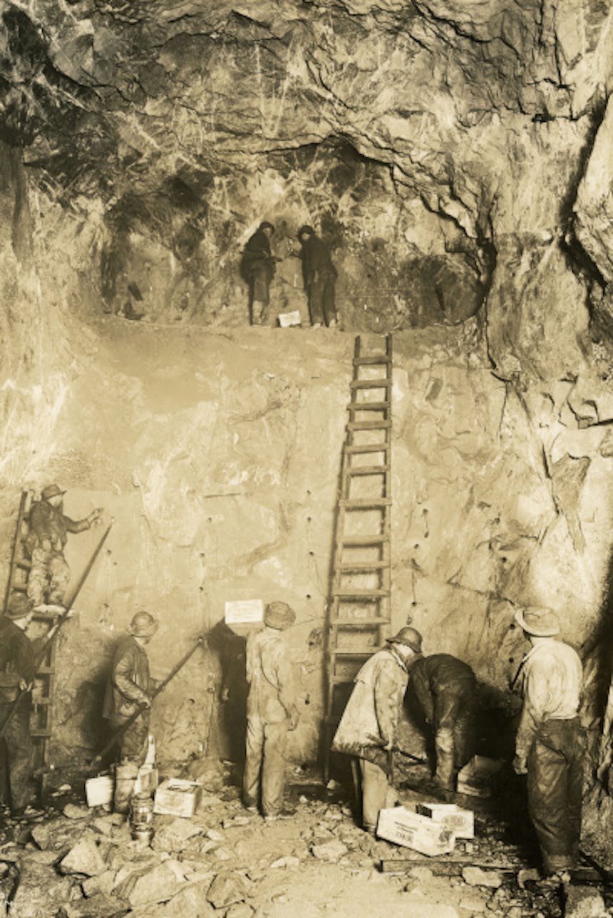 crew of men working on the great cascade tunnel drilling holes for a depth charge in a sheer stone wall with large ladder in middle