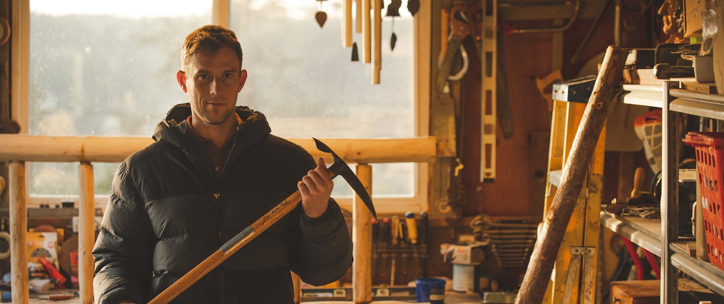 Lief Whitaker in a black parka holding his father's ice axe in an indoor workshop