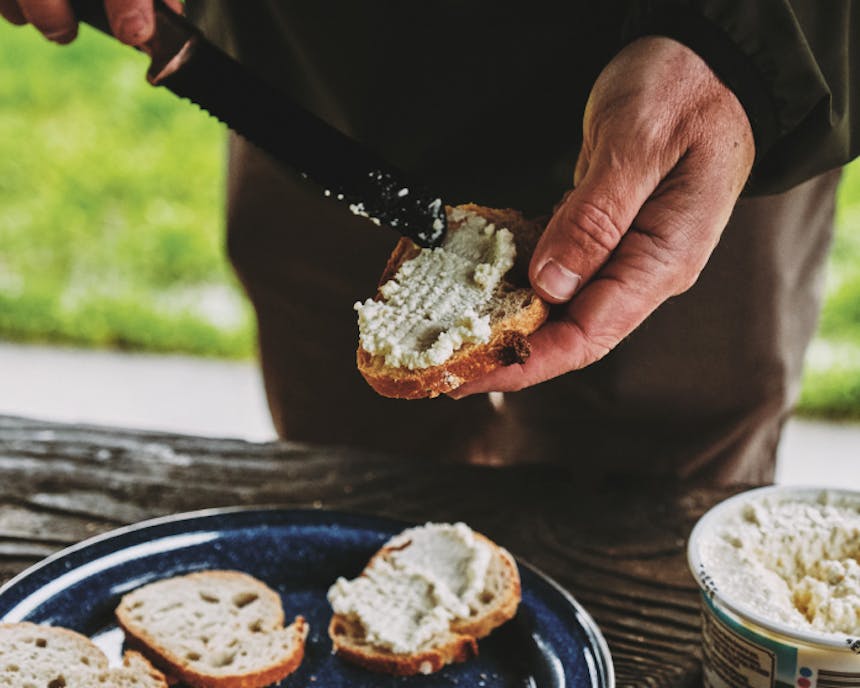 ricotta being spread on a slice of bread by a serrated knife