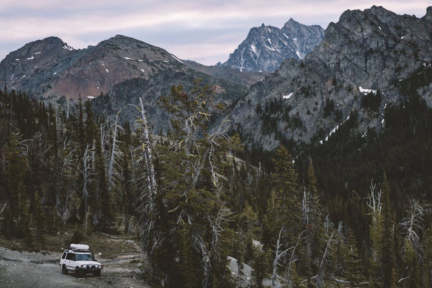 white land rover pulled over to side of gravel road in pine forest with large craggy granite mountains rising in background