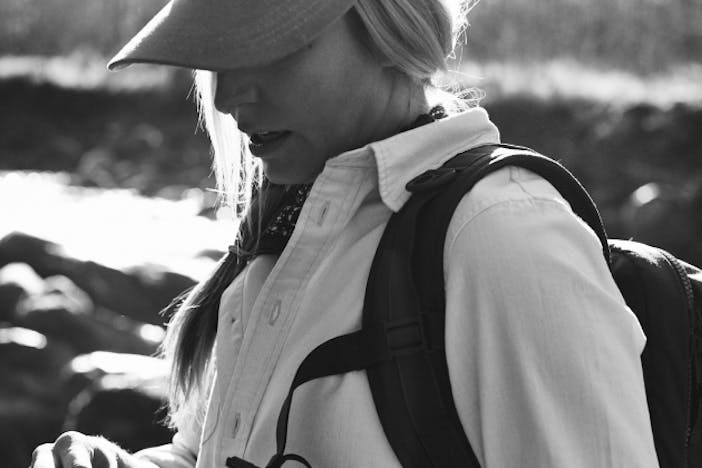 blonde woman in white shirt wearing a hat and backpack