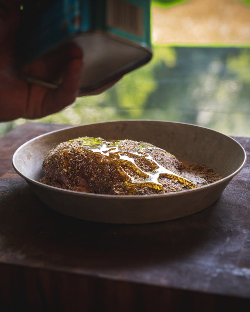 olive oil being poured on top of a dry rubbed venison sirloin in a shallow circular metal dish