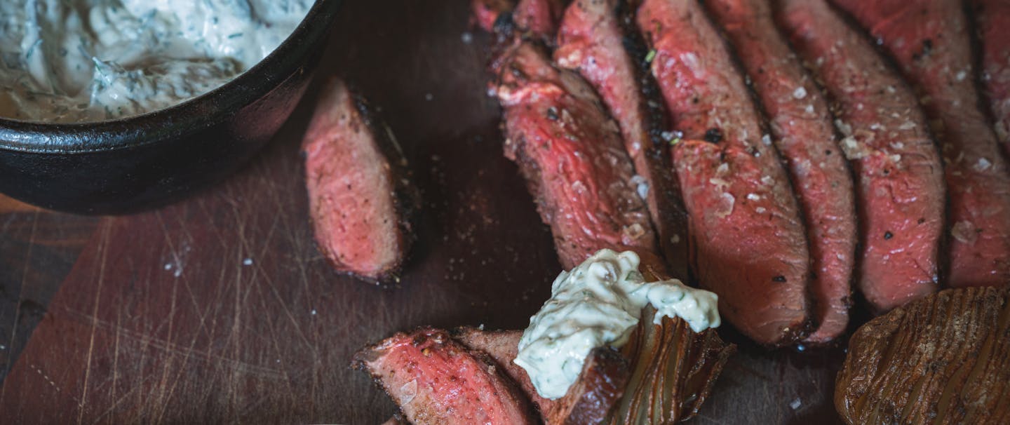 sliced venison sirloin with finishing salt and white herb aioli in small bowl and on meat