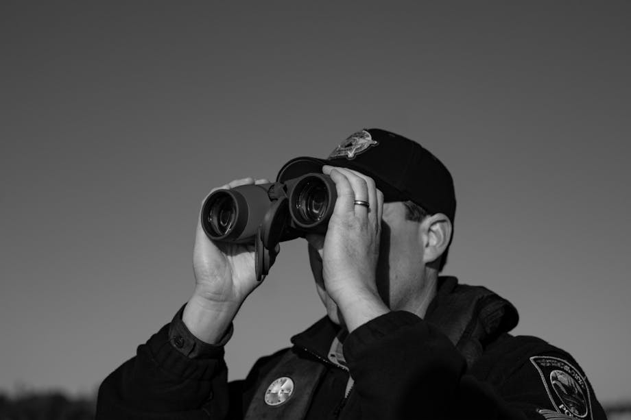 black and white image of fish and wildlife officer looking through binoculars