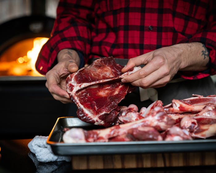 hands holding a large bone over a sheet pan with wood fired stove in background