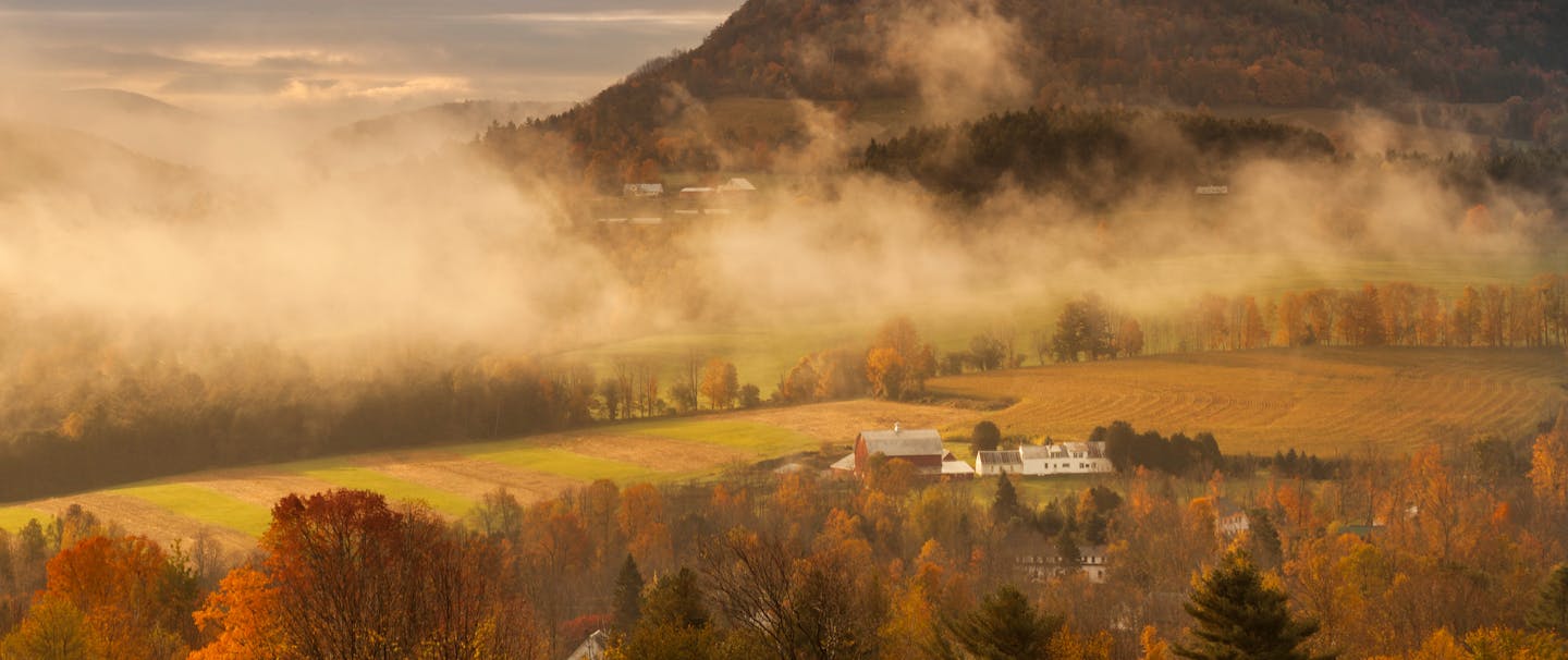 early morning light burns through the fog adding warmth and depth to this bucolic scene outside peacham, vermont
