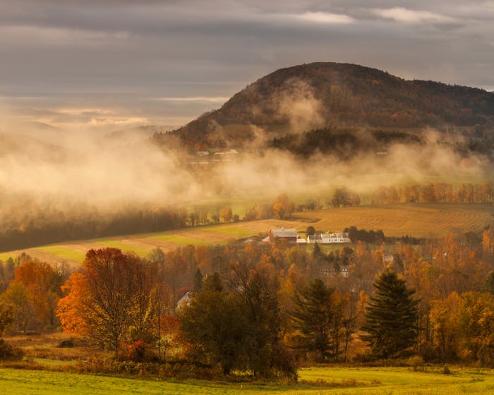 early morning light burns through the fog adding warmth and depth to this bucolic scene outside peacham, vermont