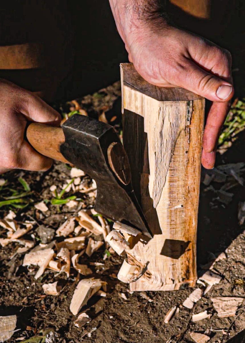 hand holding a log steady while an axe removes shavings from the interior of the log