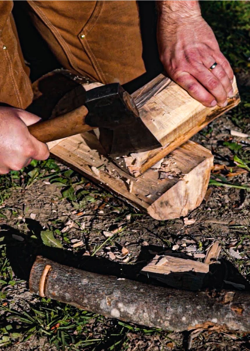 hands using an axe to remove some wood from a log