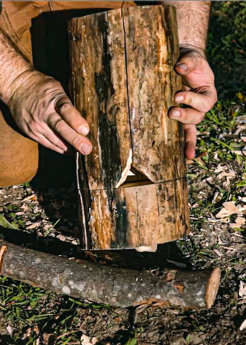 hands assembling a rocket stove out of a log with a triangular notch in the bottom half