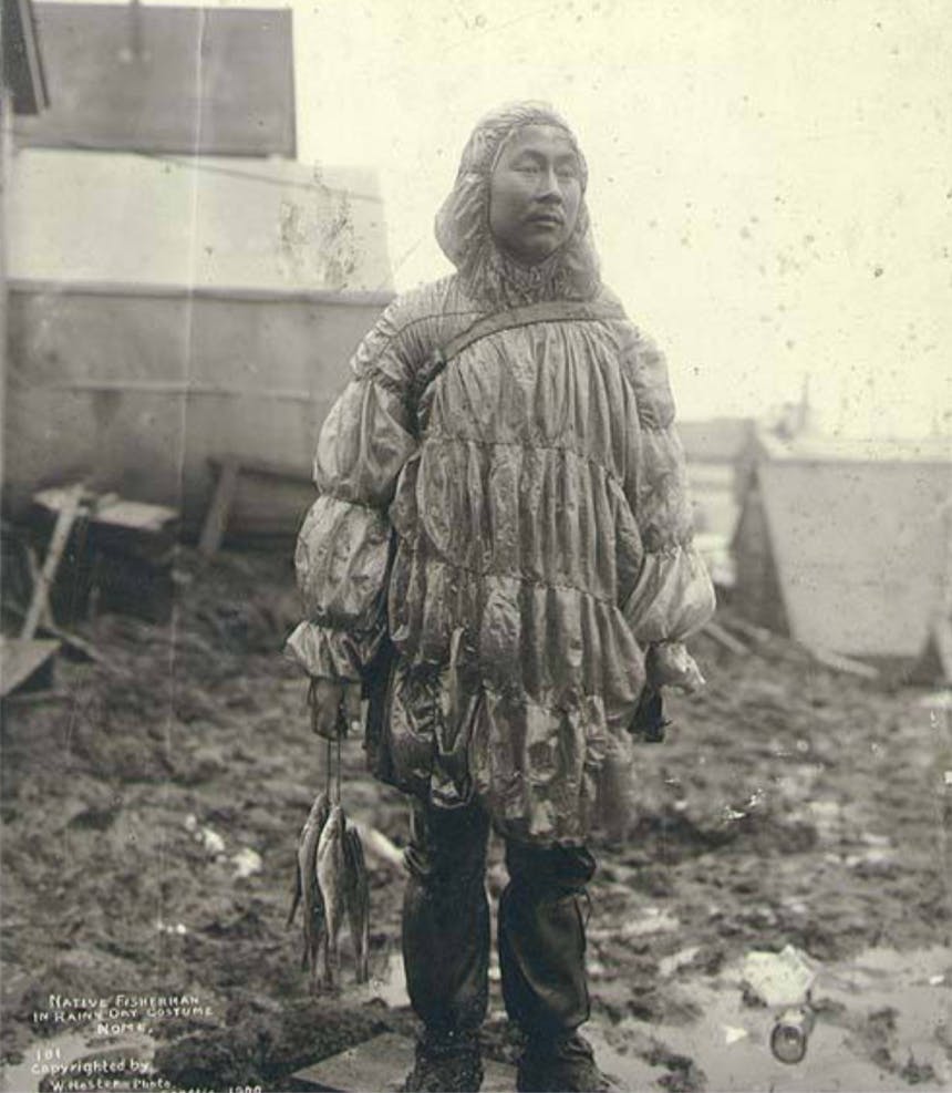 old black and white image of man holding a few fish on a line wearing a gut parka