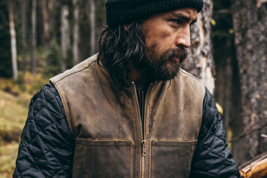 man in waxed cotton vest sitting in forest