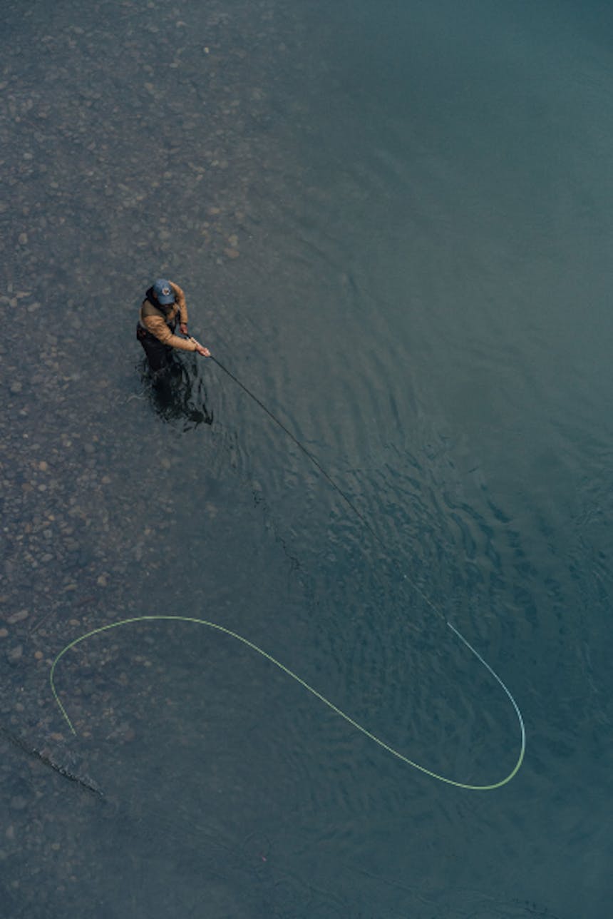 top down view of person casting a fly fishing rod while standing in shallow water