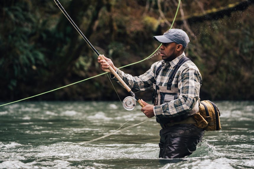 man casting fly fishing rod while wading in river