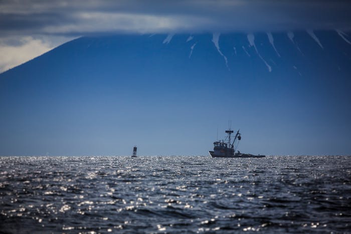 small powered boat approaches a buoy with a huge mountain looming in the background