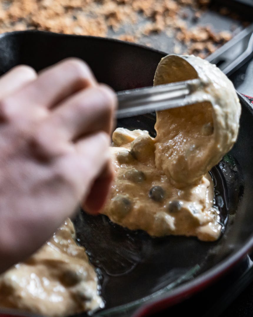 pancake batter with blueberries being ladled into a cast iron skillet