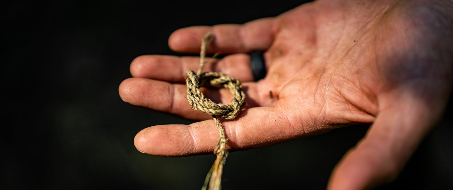 hand holding a small section of woven thin gauge rope tied in a loose knot