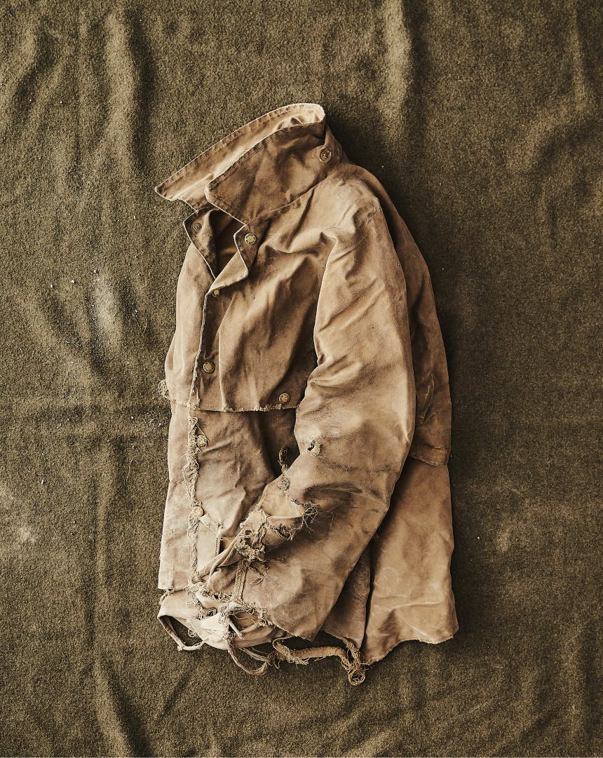 top-down view of worn tin cloth jacket laid out on an olive sheet