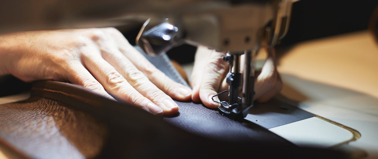 Hands guide dark leather material under the light of a sewing machine needle