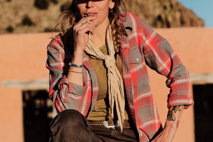 woman in gray and red plaid shirt standing in front of southwest style adobe structure