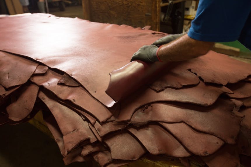 hands rolling large pieces of leather stacked on a table