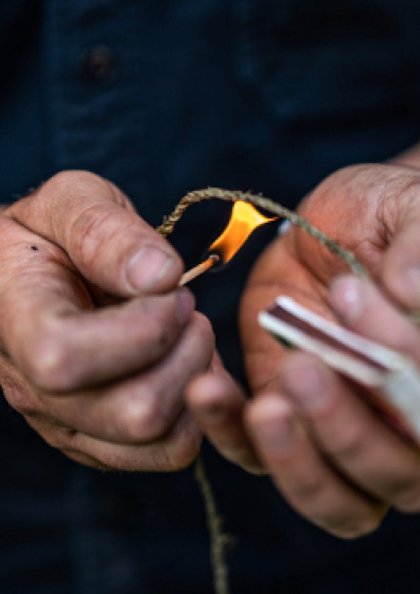 hands holding cord and a match burning off the frayed edges of stinging nettle cord