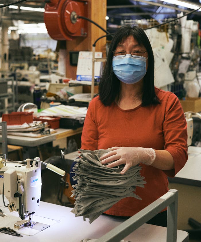 woman wearing a surgical face mask holding a stack of fabric facemasks in a textile shop