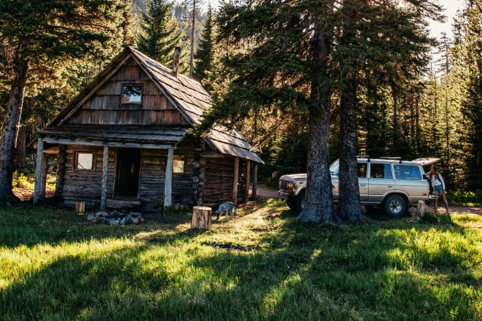 idyllic log cabin with gold bronco parked outside in a pine forest meadow