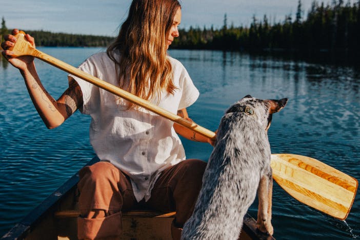 woman in white shirt holding a wooden oar sitting in a canoe next to an australian shepherd