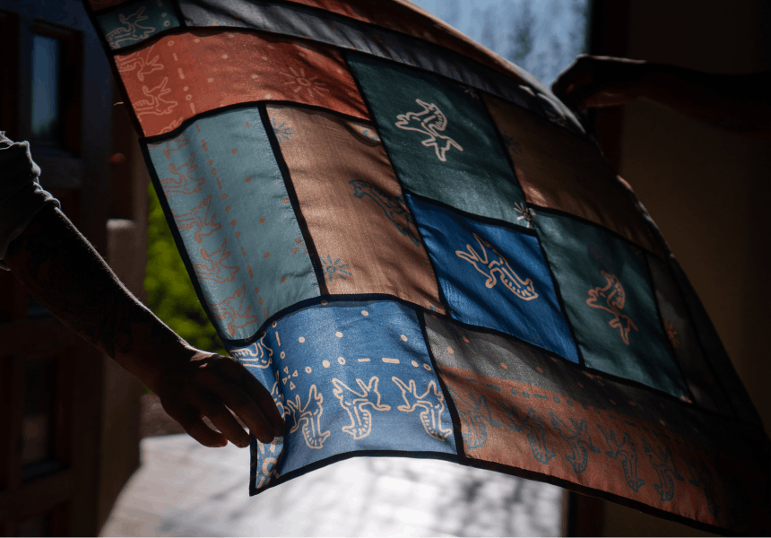 hand holding a piece of cloth with various colors and designs with sun shining through it
